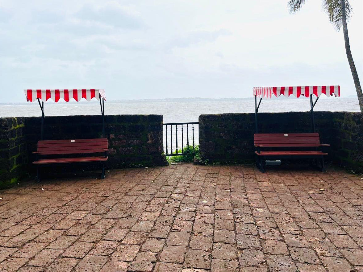 unWOOD benches with striped canopies on a stone pathway near a body of water.